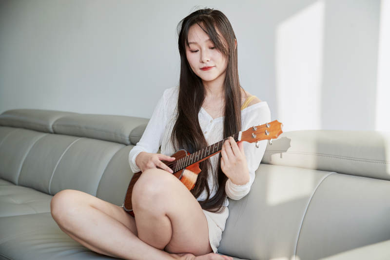 坐在沙发上弹奏尤克里里的少女图片