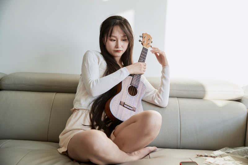坐在沙发上弹奏尤克里里的少女图片