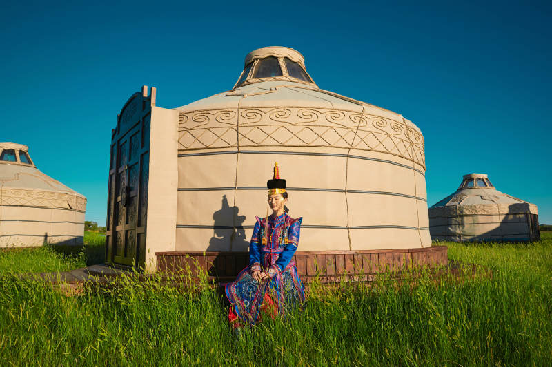 夕阳下草原蒙古大帐前穿蒙族服饰的美女图片