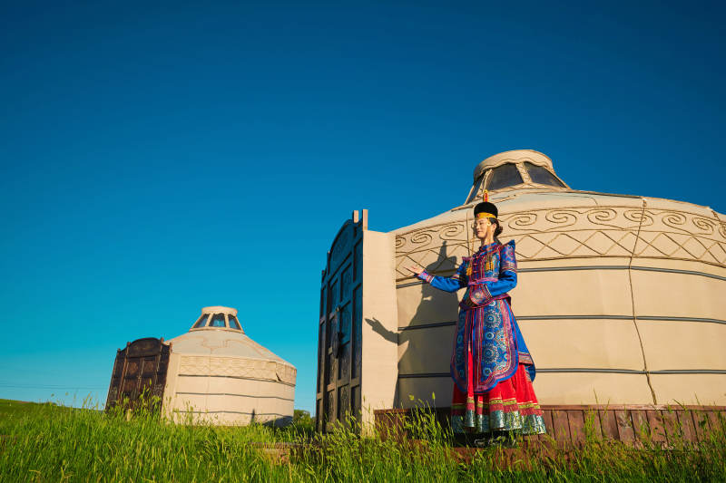 夕阳下草原蒙古大帐前穿蒙族服饰的美女图片