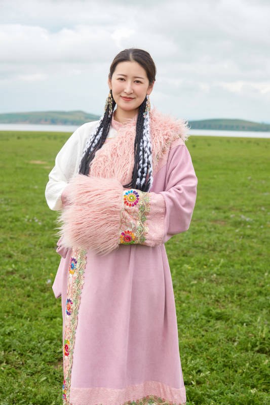 身穿粉色藏族服饰在草原拍照的少女图片