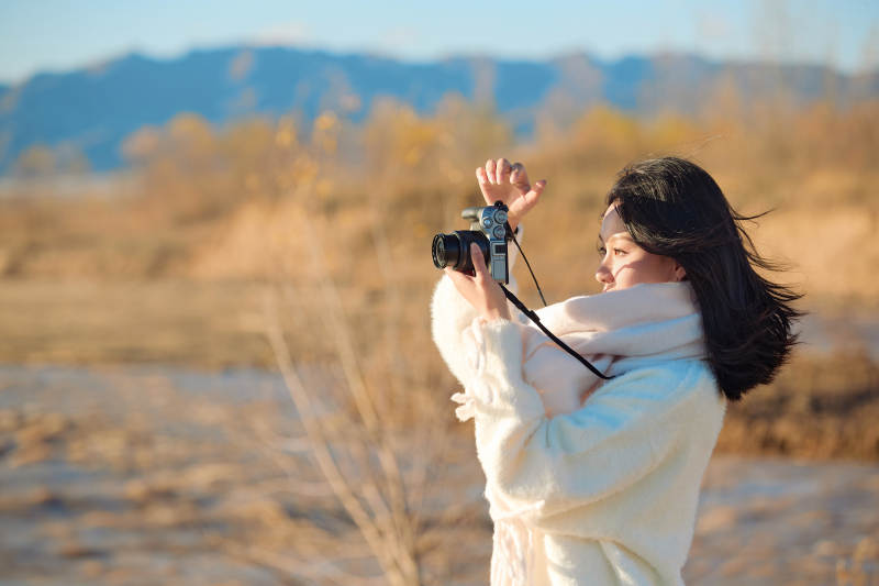 拿着相机的美女摄影师在深秋的户外拍摄图片