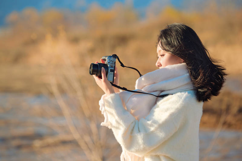 拿着相机的美女摄影师在深秋的户外拍摄图片