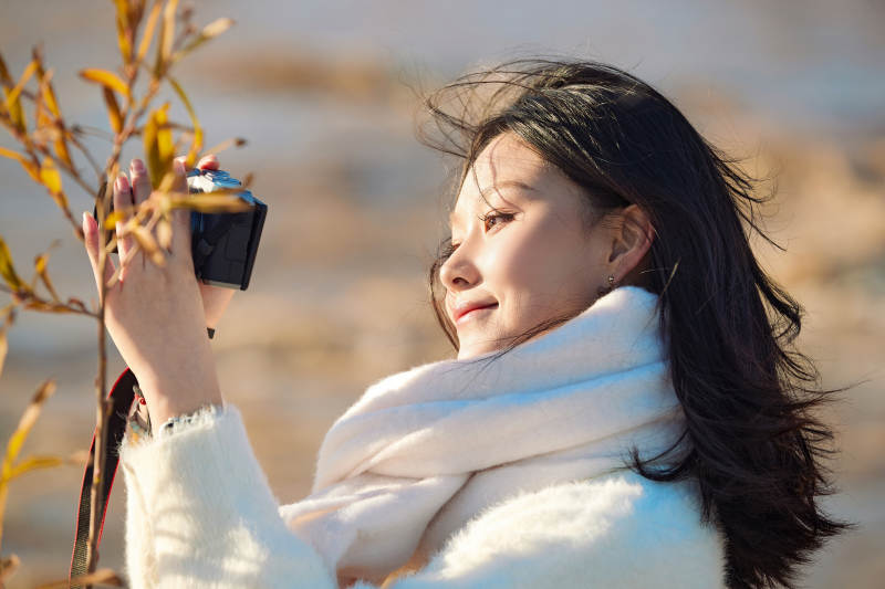 拿着相机的美女摄影师在深秋的户外拍摄图片