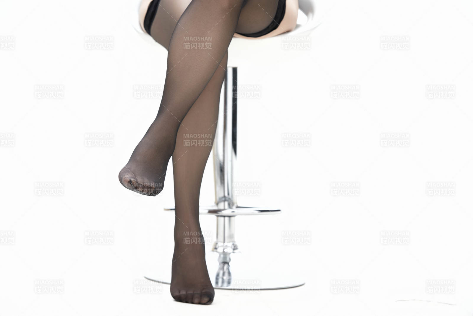 在白色背景上穿着黑色长袜的女人的苗条的腿图片
