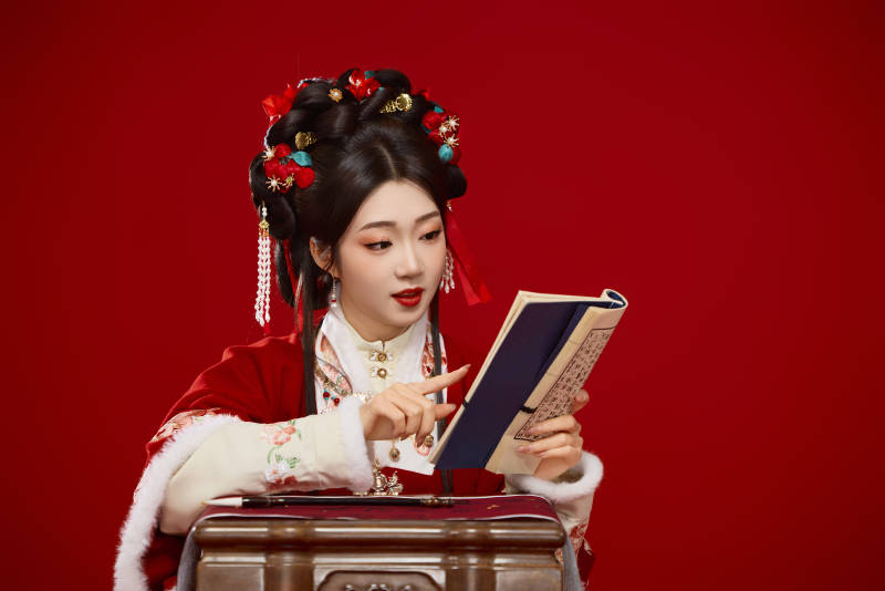 红色背景下身穿喜庆汉服认真学习的中国美女图片