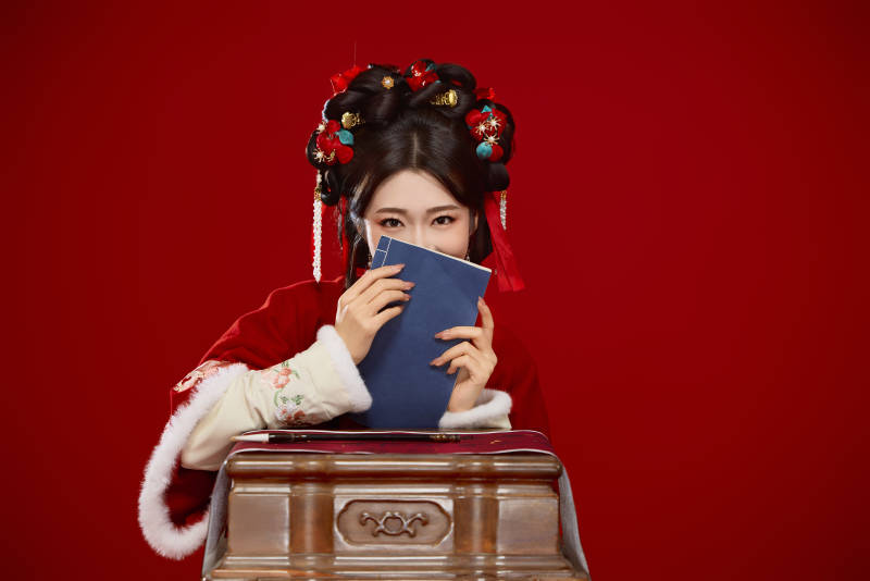 红色背景下身穿喜庆汉服认真学习的中国美女图片