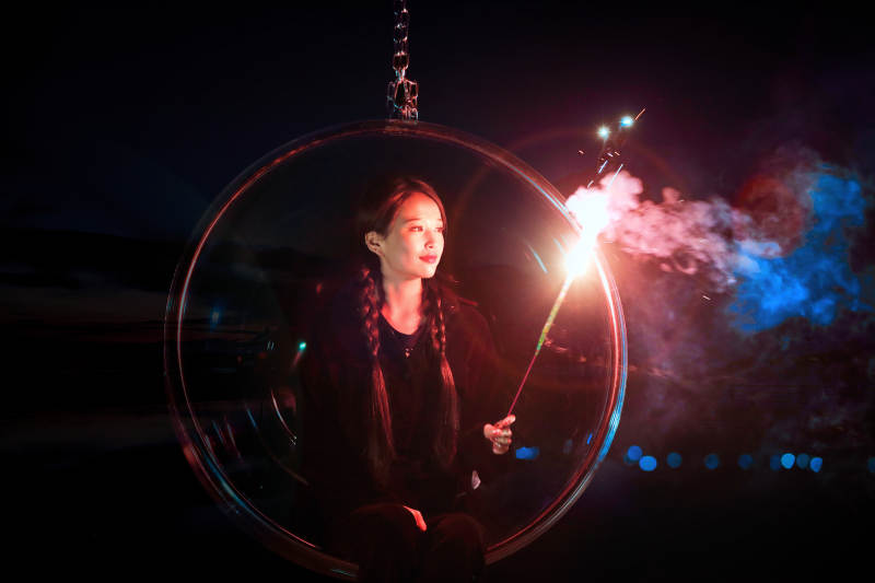 夜晚坐在透明秋千上燃放仙女棒的可爱少女图片