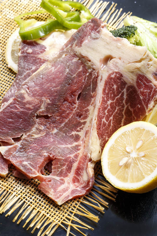 黑色背景草垫上的T骨牛排配柠檬图片