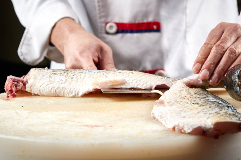 白色砧板上厨师用精湛的刀工展示生鱼片及鲜鱼料理切割分切的刀工图片