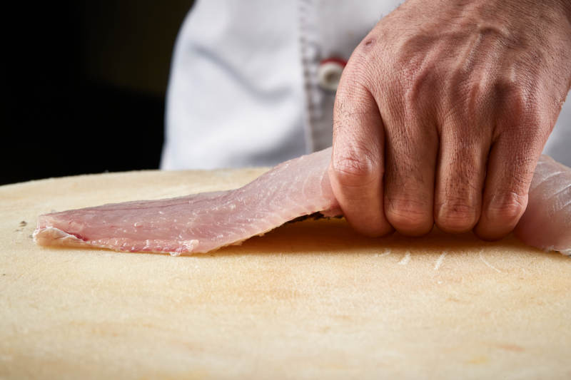 白色砧板上厨师用精湛的刀工展示生鱼片及鲜鱼料理切割分切的刀工图片