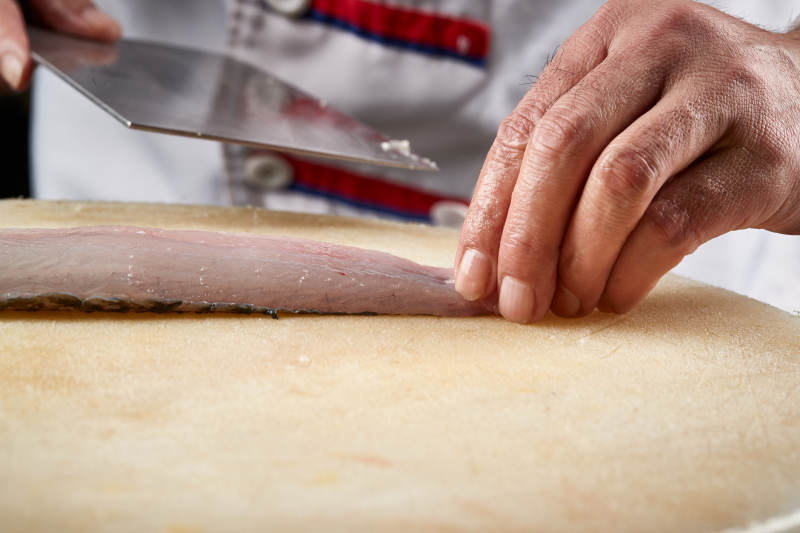 白色砧板上厨师用精湛的刀工展示生鱼片及鲜鱼料理切割分切的刀工图片