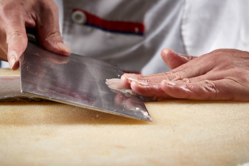 白色砧板上厨师用精湛的刀工展示生鱼片及鲜鱼料理切割分切的刀工图片