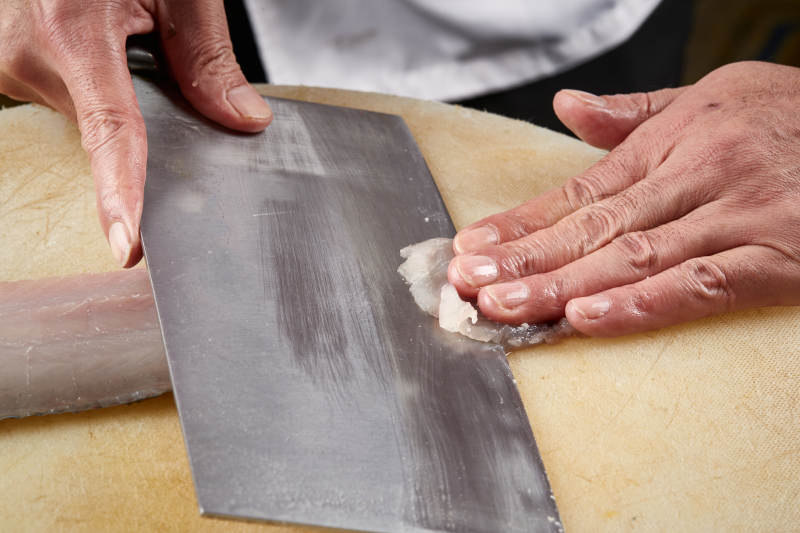 白色砧板上厨师用精湛的刀工展示生鱼片及鲜鱼料理切割分切的刀工图片