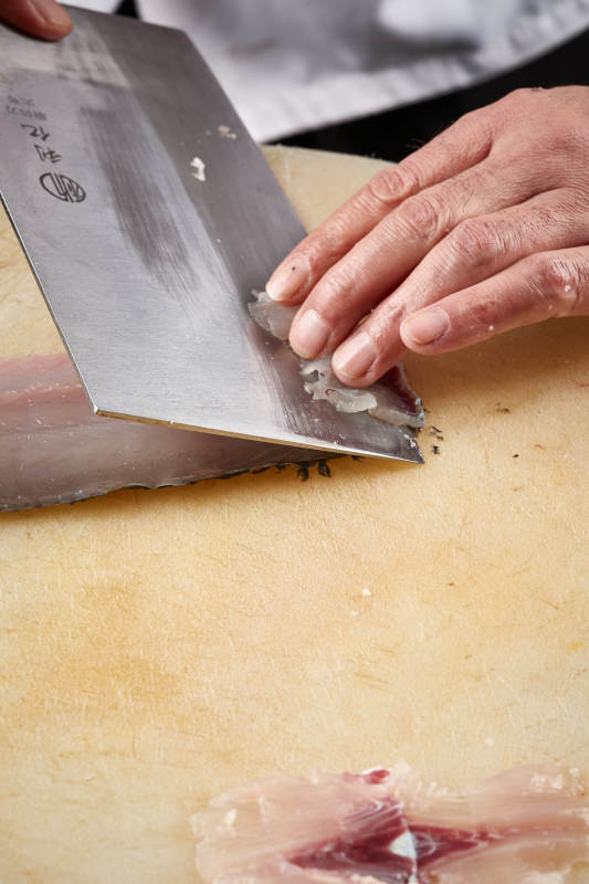 白色砧板上厨师用精湛的刀工展示生鱼片及鲜鱼料理切割分切的刀工图片