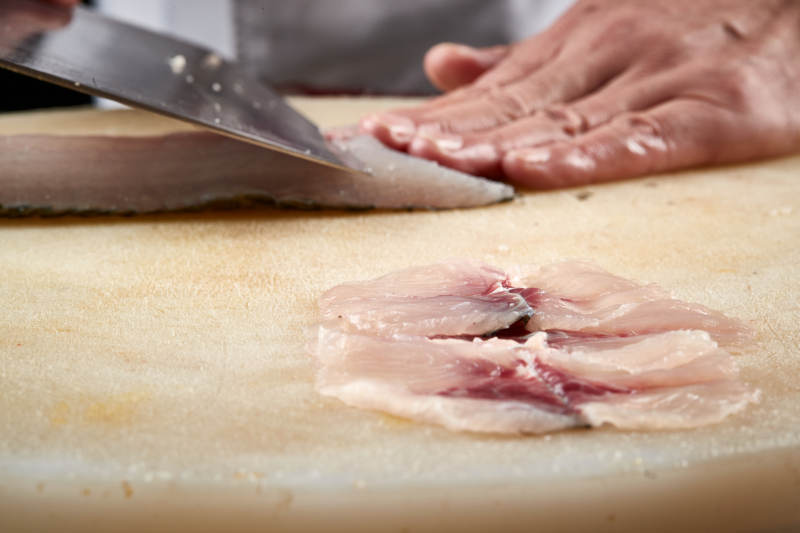 白色砧板上厨师用精湛的刀工展示生鱼片及鲜鱼料理切割分切的刀工图片