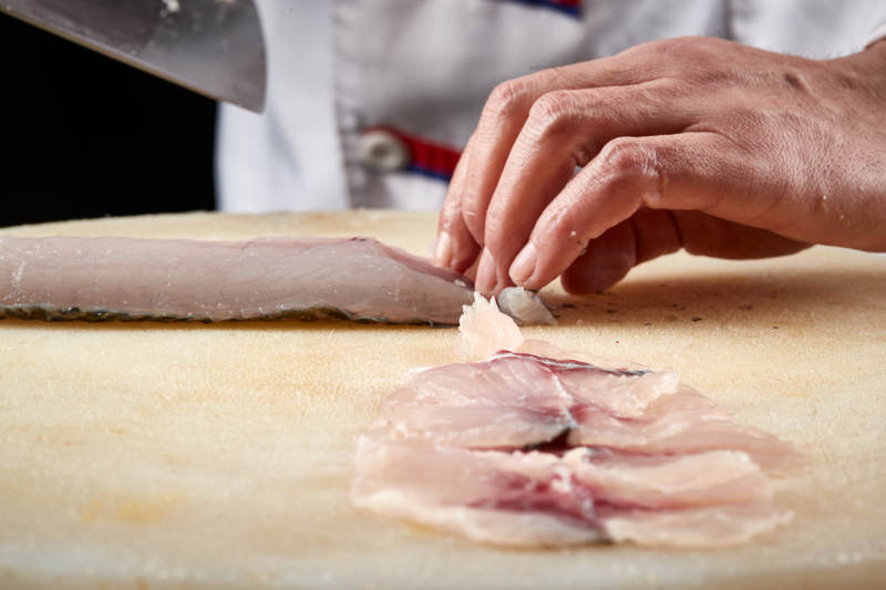 白色砧板上厨师用精湛的刀工展示生鱼片及鲜鱼料理切割分切的刀工图片