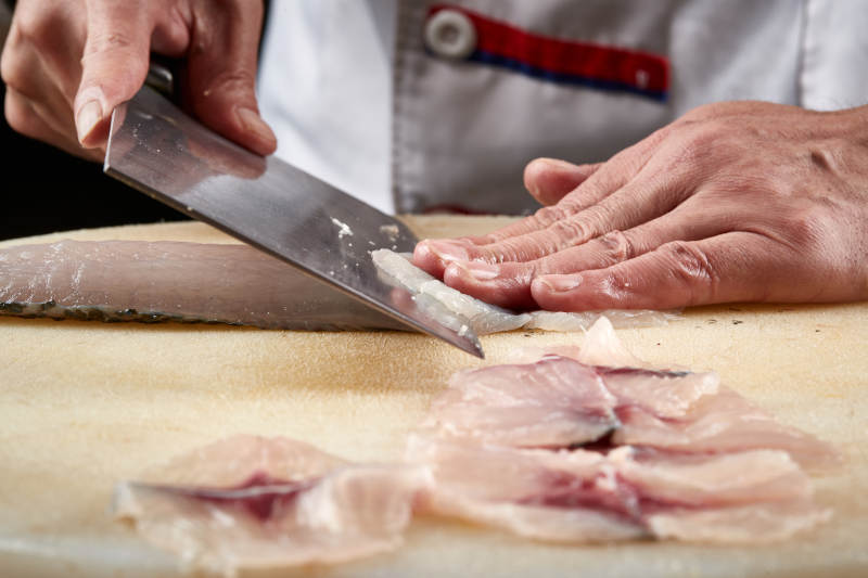 白色砧板上厨师用精湛的刀工展示生鱼片及鲜鱼料理切割分切的刀工图片