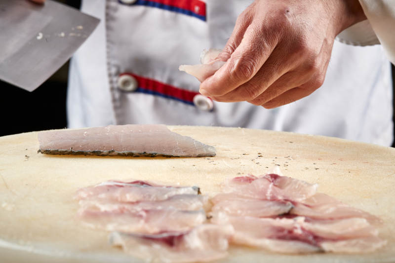 白色砧板上厨师用精湛的刀工展示生鱼片及鲜鱼料理切割分切的刀工图片