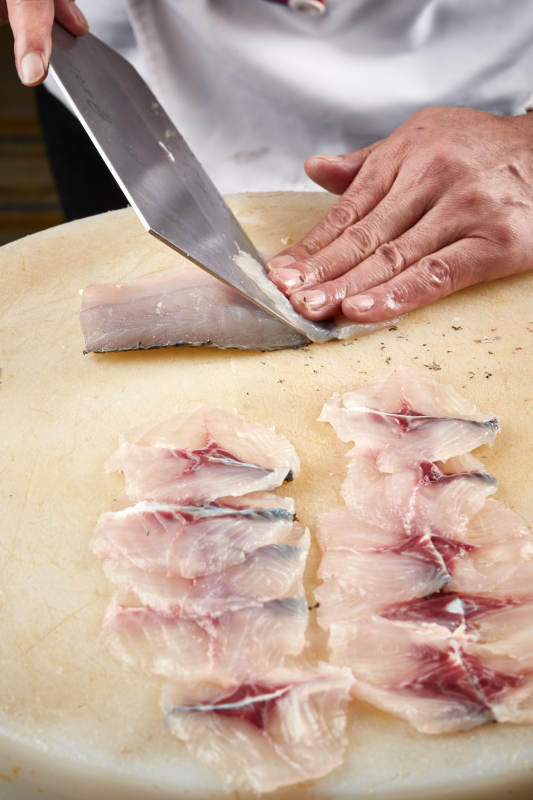 白色砧板上厨师用精湛的刀工展示生鱼片及鲜鱼料理切割分切的刀工图片