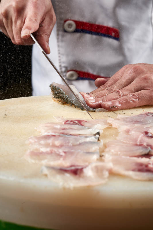 白色砧板上厨师用精湛的刀工展示生鱼片及鲜鱼料理切割分切的刀工图片