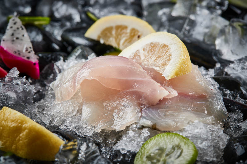 将晶莹白润的鲜鱼片码放在黑色的圆瓷盘上图片