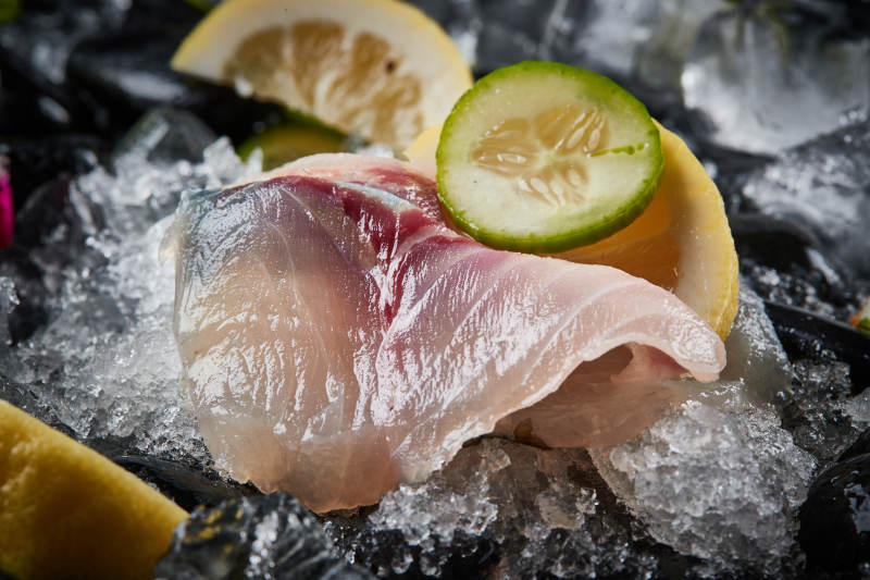 将晶莹白润的鲜鱼片码放在黑色的圆瓷盘上图片