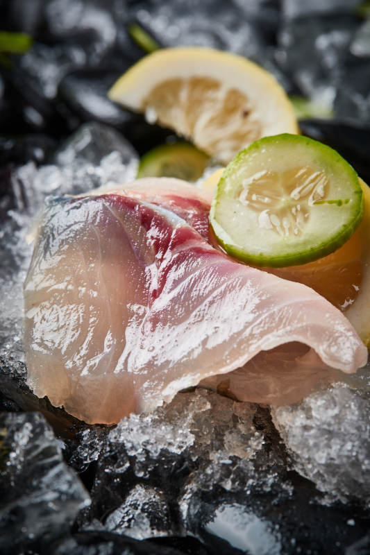 将晶莹白润的鲜鱼片码放在黑色的圆瓷盘上图片