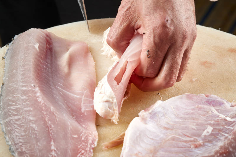 白色砧板上厨师用精湛的刀工展示生鱼片及鲜鱼料理切割分切的刀工图片