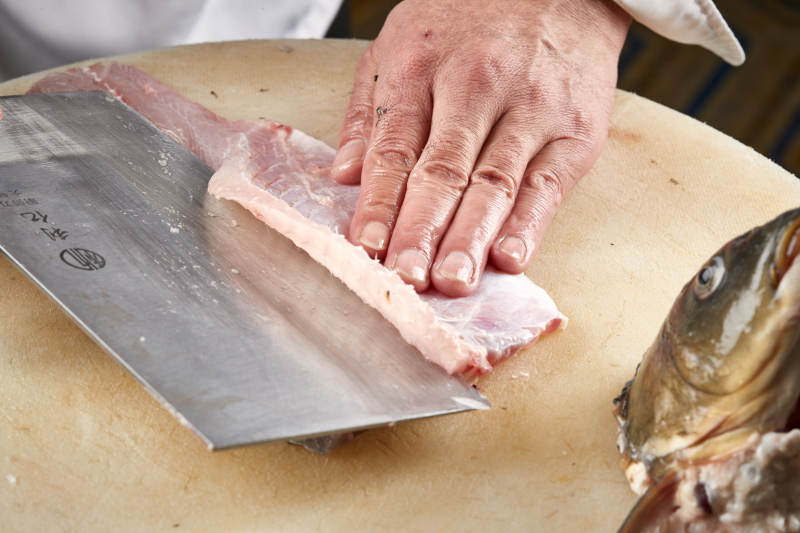 白色砧板上厨师用精湛的刀工展示生鱼片及鲜鱼料理切割分切的刀工图片