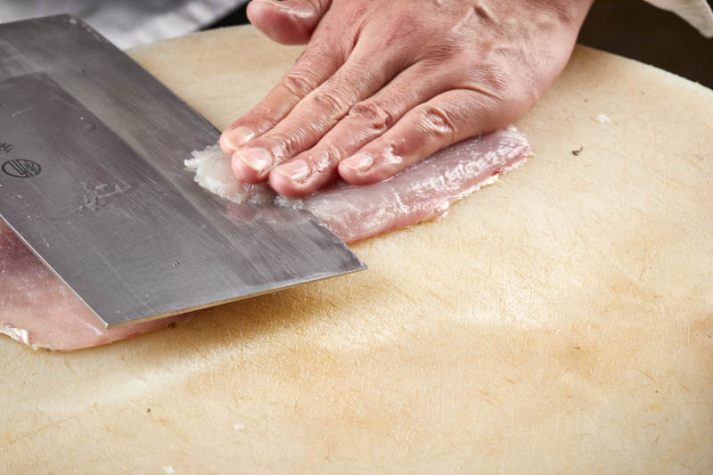 白色砧板上厨师用精湛的刀工展示生鱼片及鲜鱼料理切割分切的刀工图片