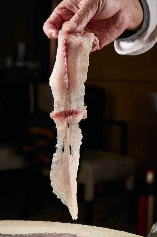 白色砧板上厨师用精湛的刀工展示生鱼片及鲜鱼料理切割分切的刀工图片