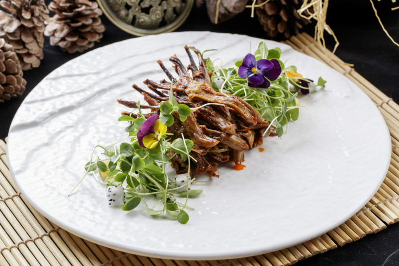 寿司帘上的圆瓷盘装的香辣鸭舌图片