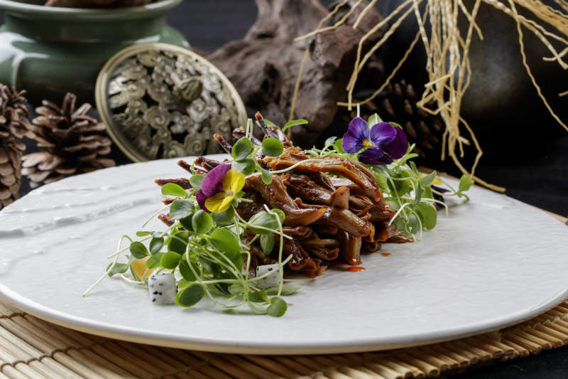 寿司帘上的圆瓷盘装的香辣鸭舌图片