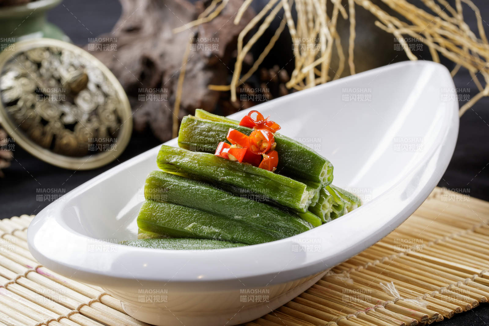 寿司帘上的元宝形瓷盘装的浇汁秋葵图片