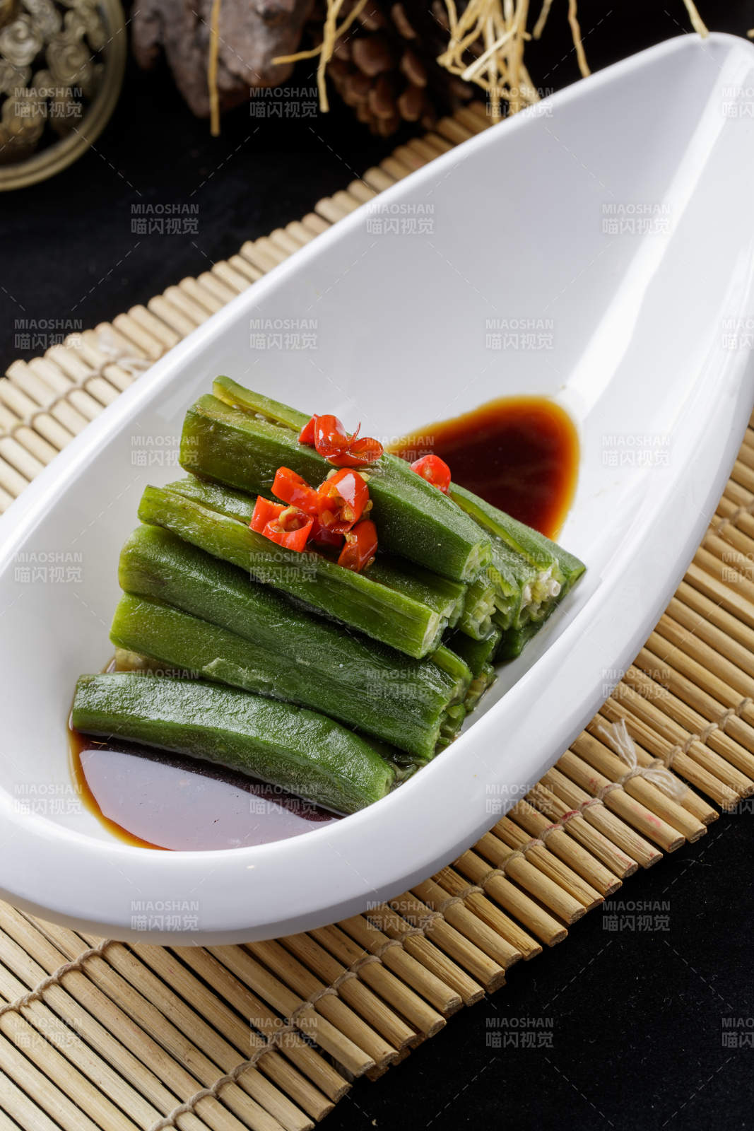 寿司帘上的元宝形瓷盘装的浇汁秋葵图片