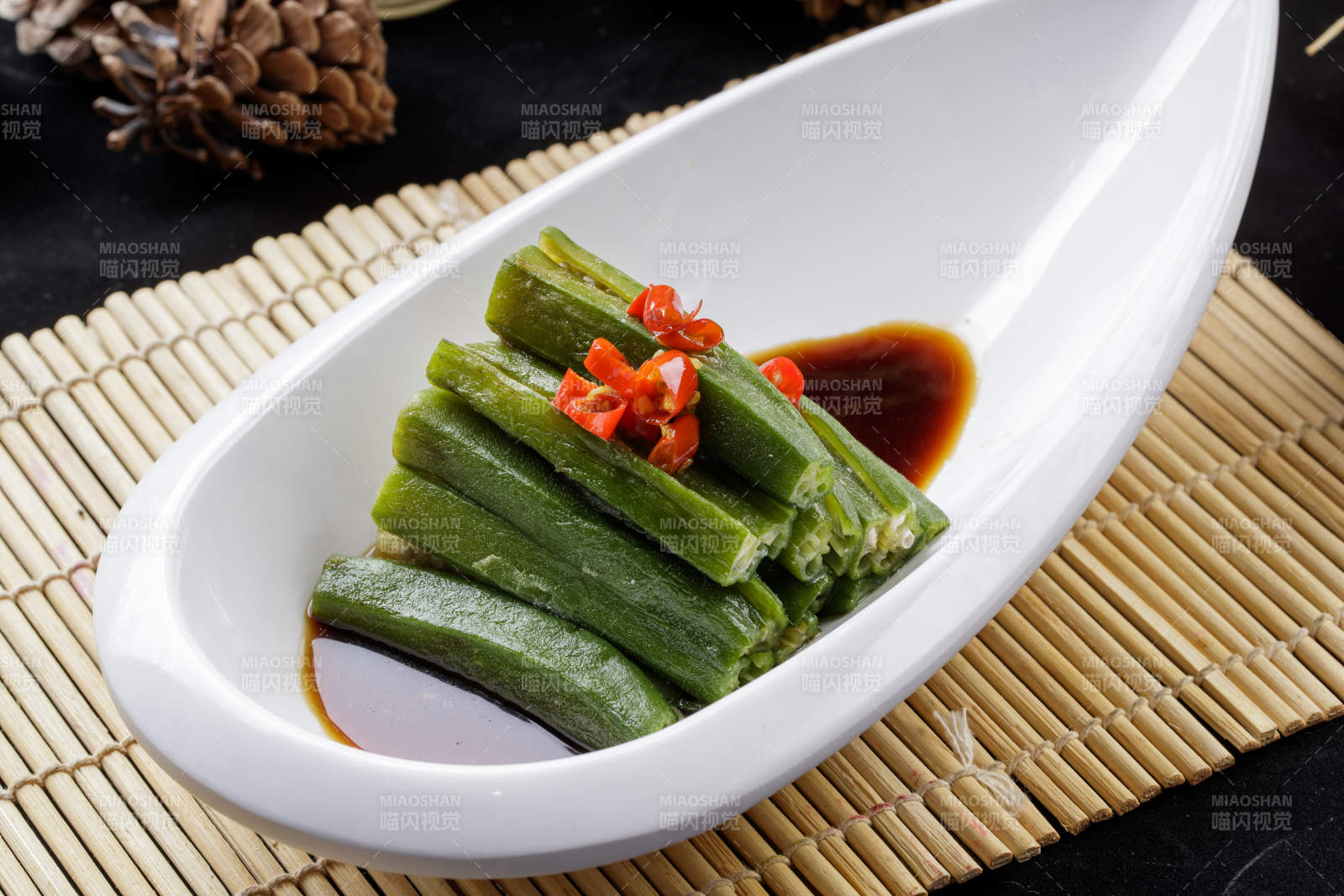寿司帘上的元宝形瓷盘装的浇汁秋葵图片