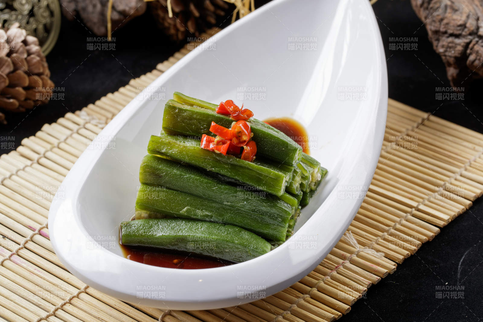 寿司帘上的元宝形瓷盘装的浇汁秋葵图片