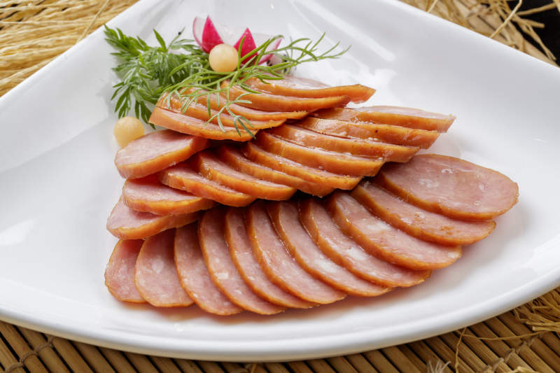 寿司帘上的扇形瓷盘装的自制蒜味香肠图片