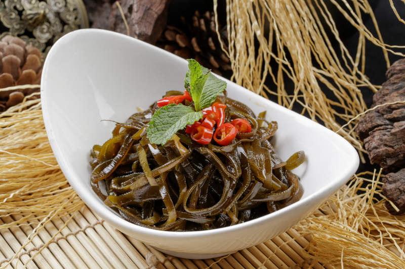 寿司帘上的元宝瓷盘装的凉拌海带丝图片