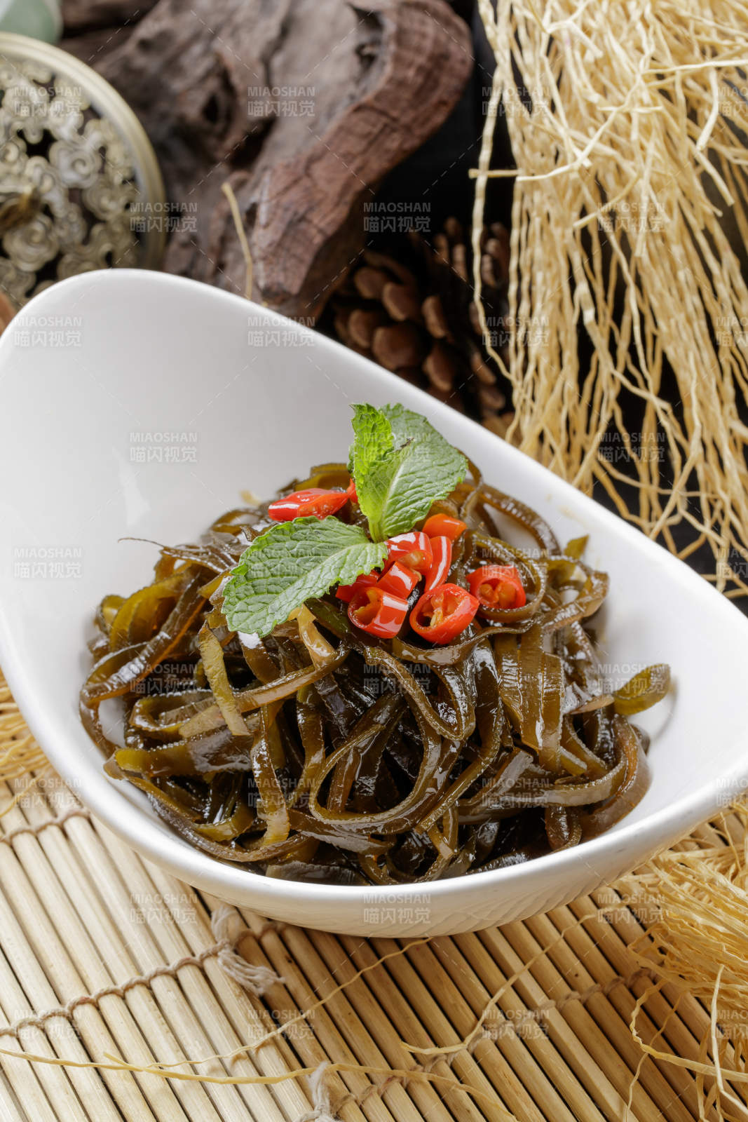 寿司帘上的元宝瓷盘装的凉拌海带丝图片