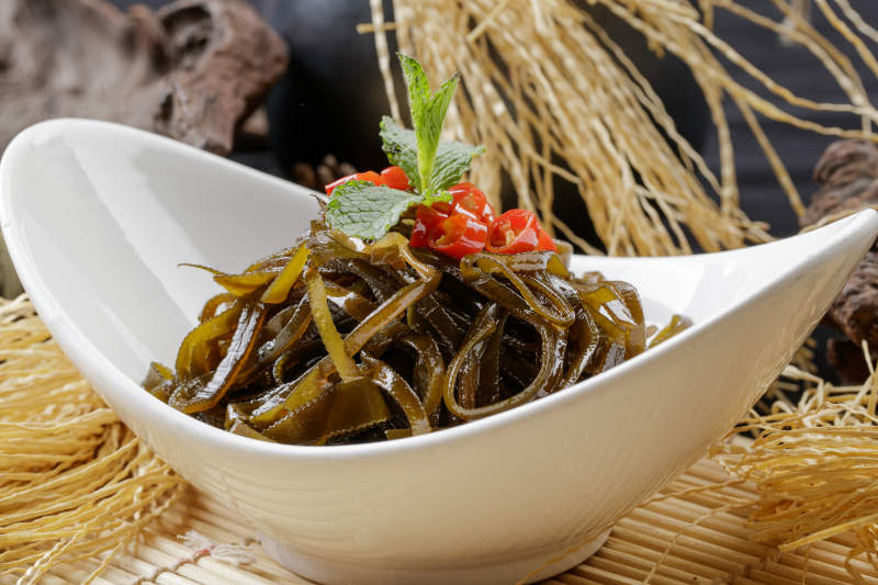 寿司帘上的元宝瓷盘装的凉拌海带丝图片