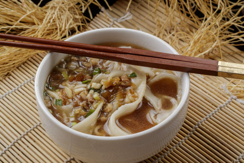 寿司帘上的白瓷碗装的茄丁打卤面图片