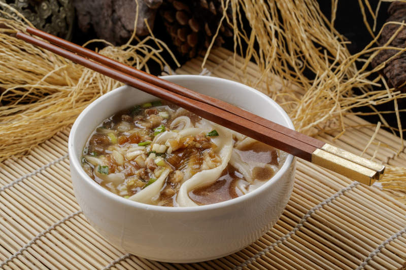 寿司帘上的白瓷碗装的茄丁打卤面图片