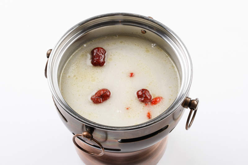 白色背景上的小火锅装的大骨奶汤锅底图片