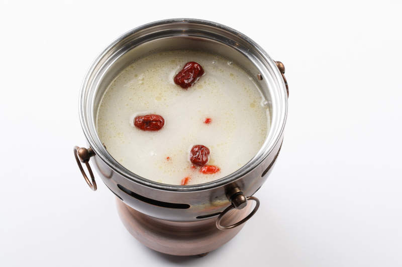 白色背景上的小火锅装的大骨奶汤锅底图片