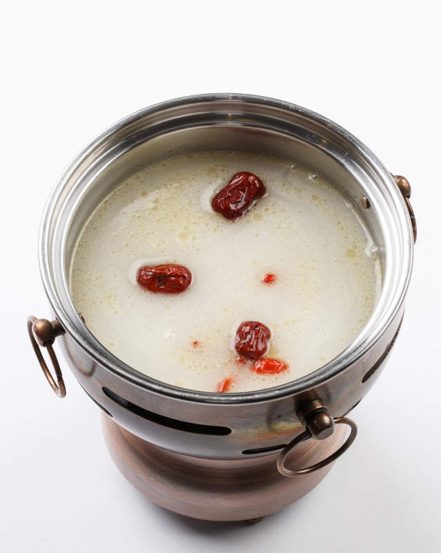 白色背景上的小火锅装的大骨奶汤锅底图片