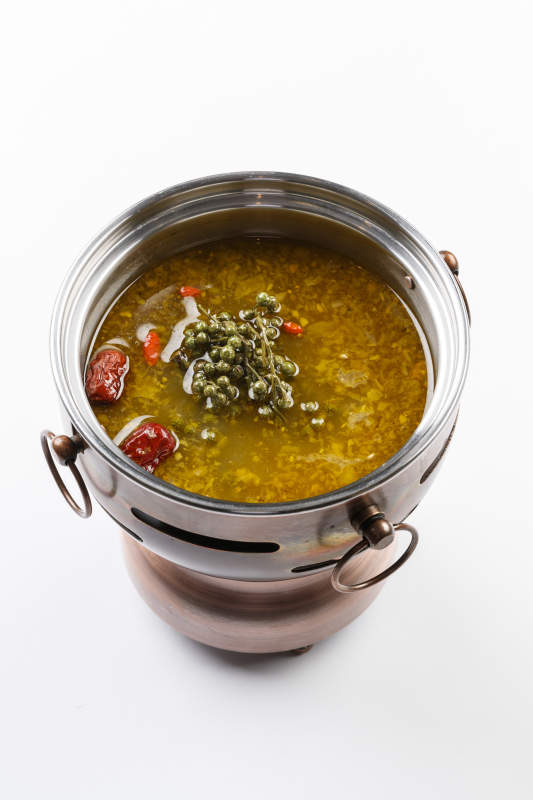 白色背景上的小火锅装的牛油藤椒酸辣锅底图片