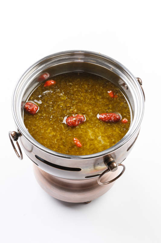 白色背景上的小火锅装的雪菜牛油锅底图片