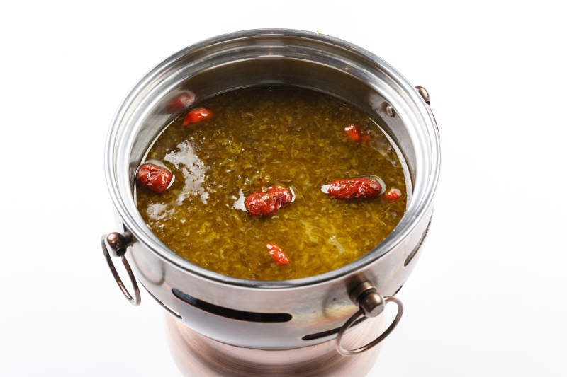 白色背景上的小火锅装的雪菜牛油锅底图片